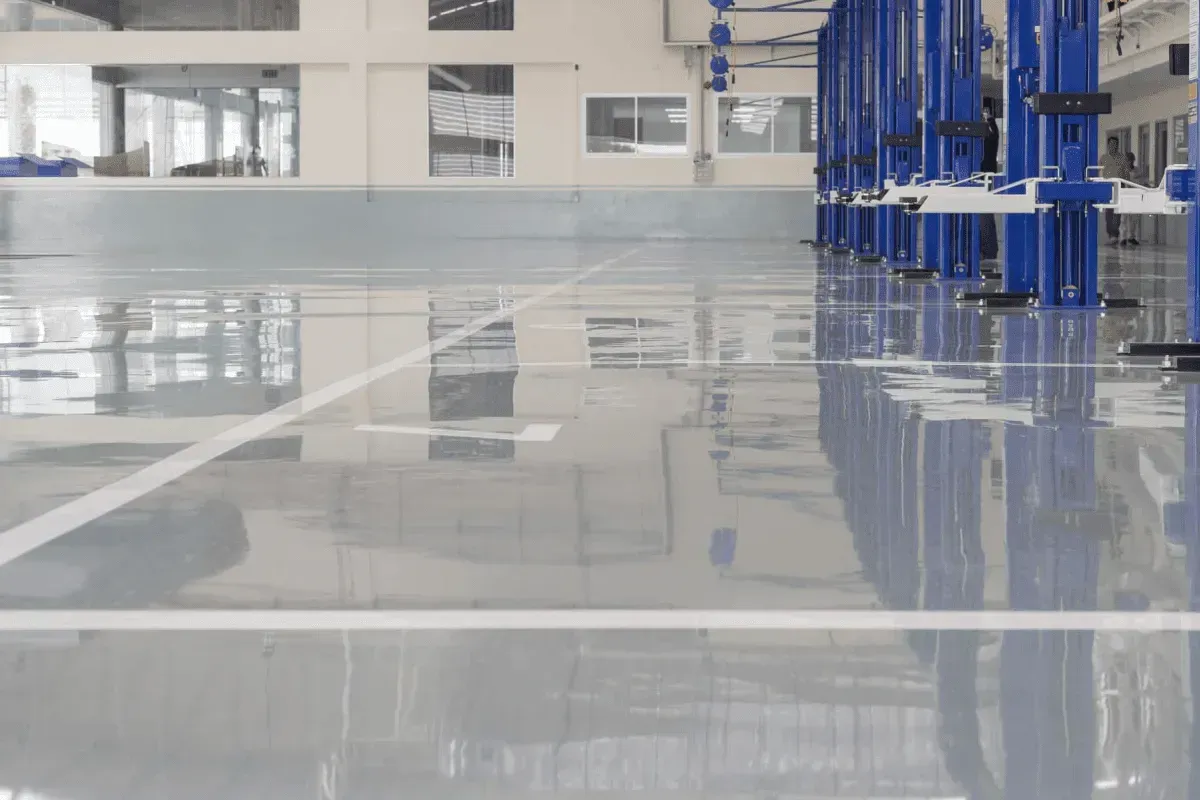 Glossy gray industrial floor with white lines, blue equipment in the background.