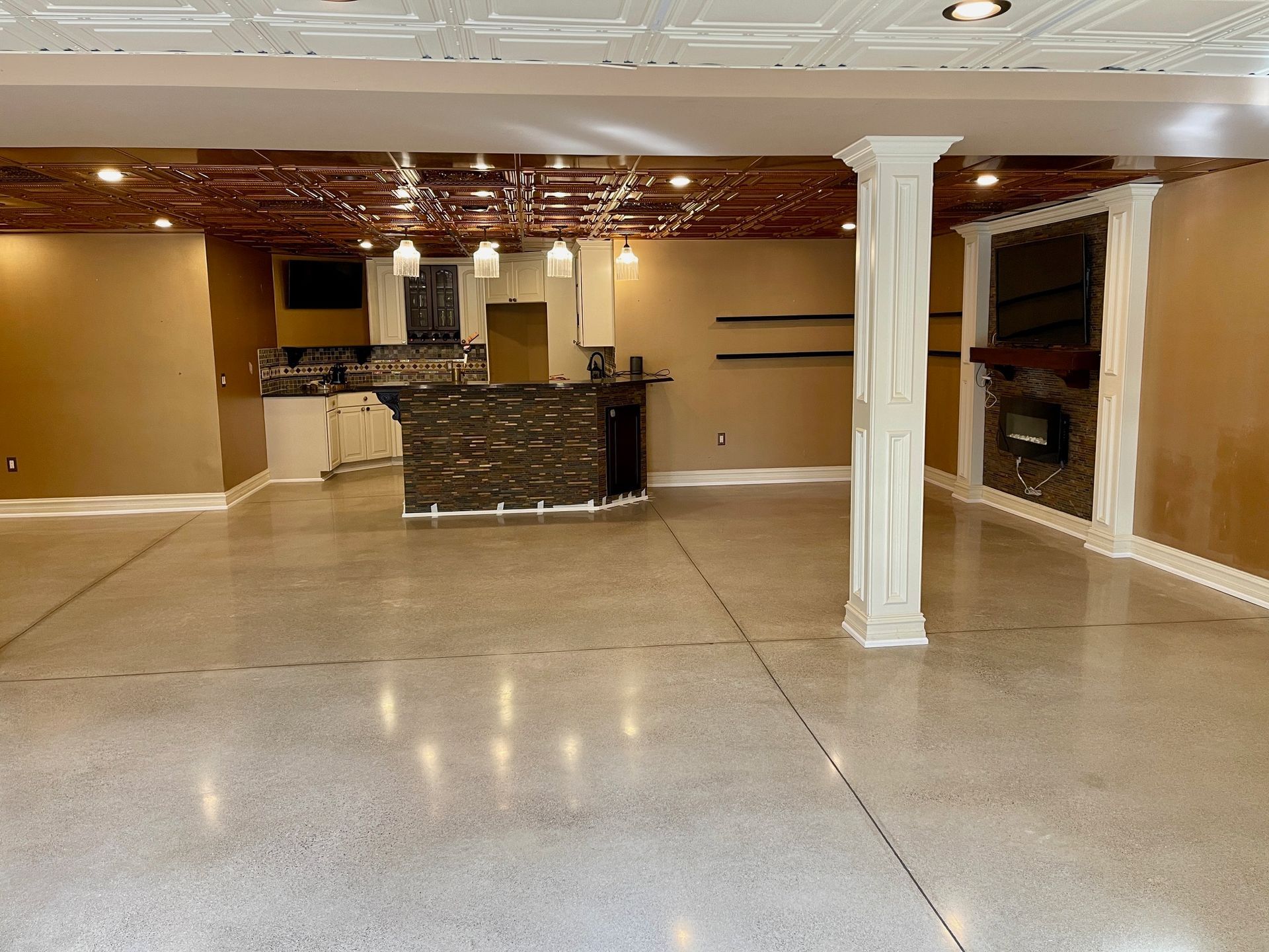 Spacious, unfinished basement with bar, fireplace, columns, and polished concrete floor.