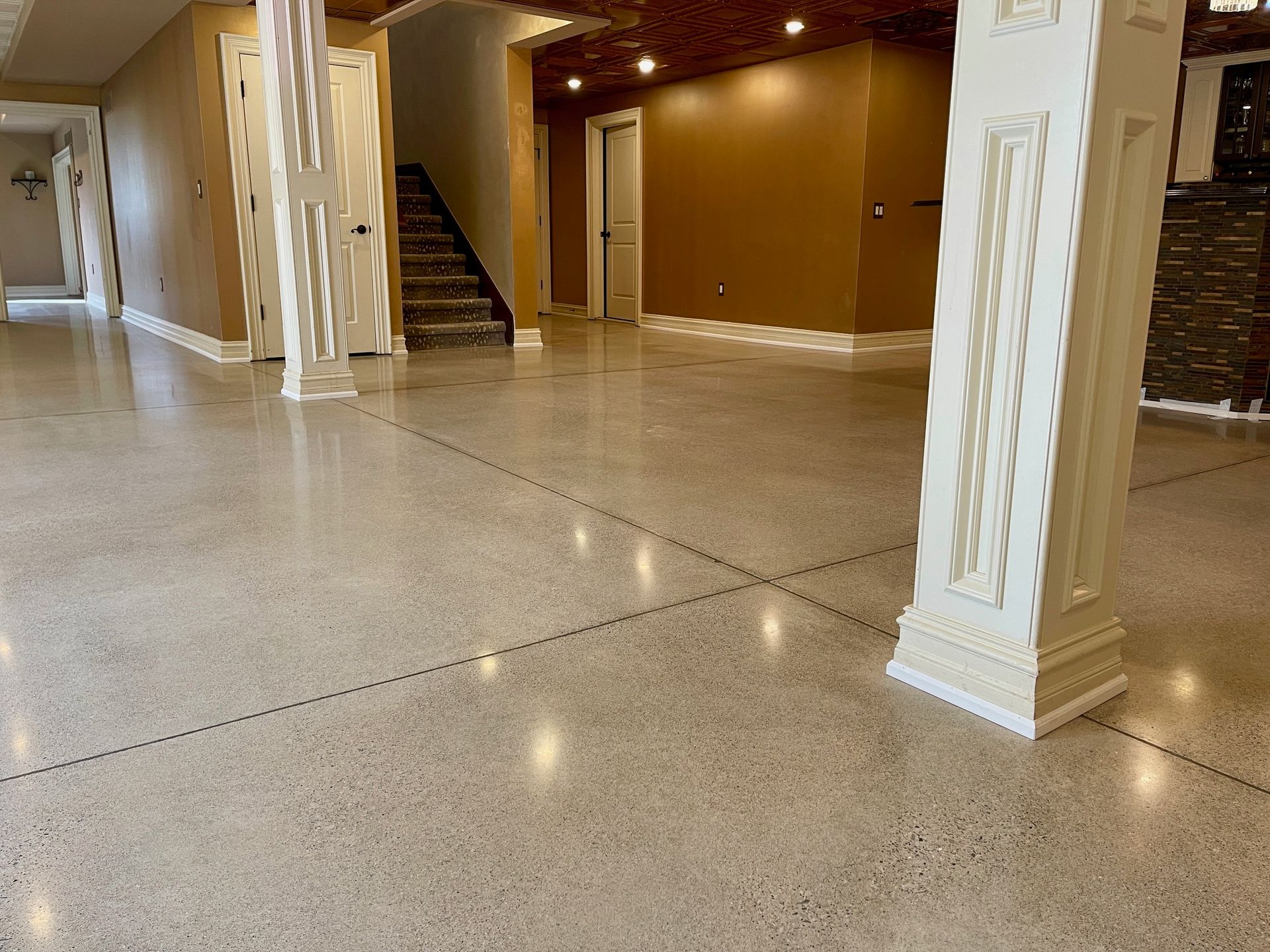 Polished concrete floor in a large room, with columns and stairs. Beige and brown tones.