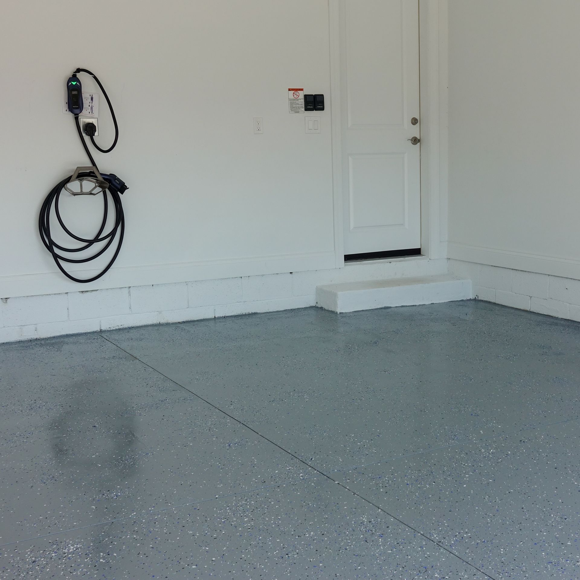Gray epoxy garage floor with a door and EV charger.