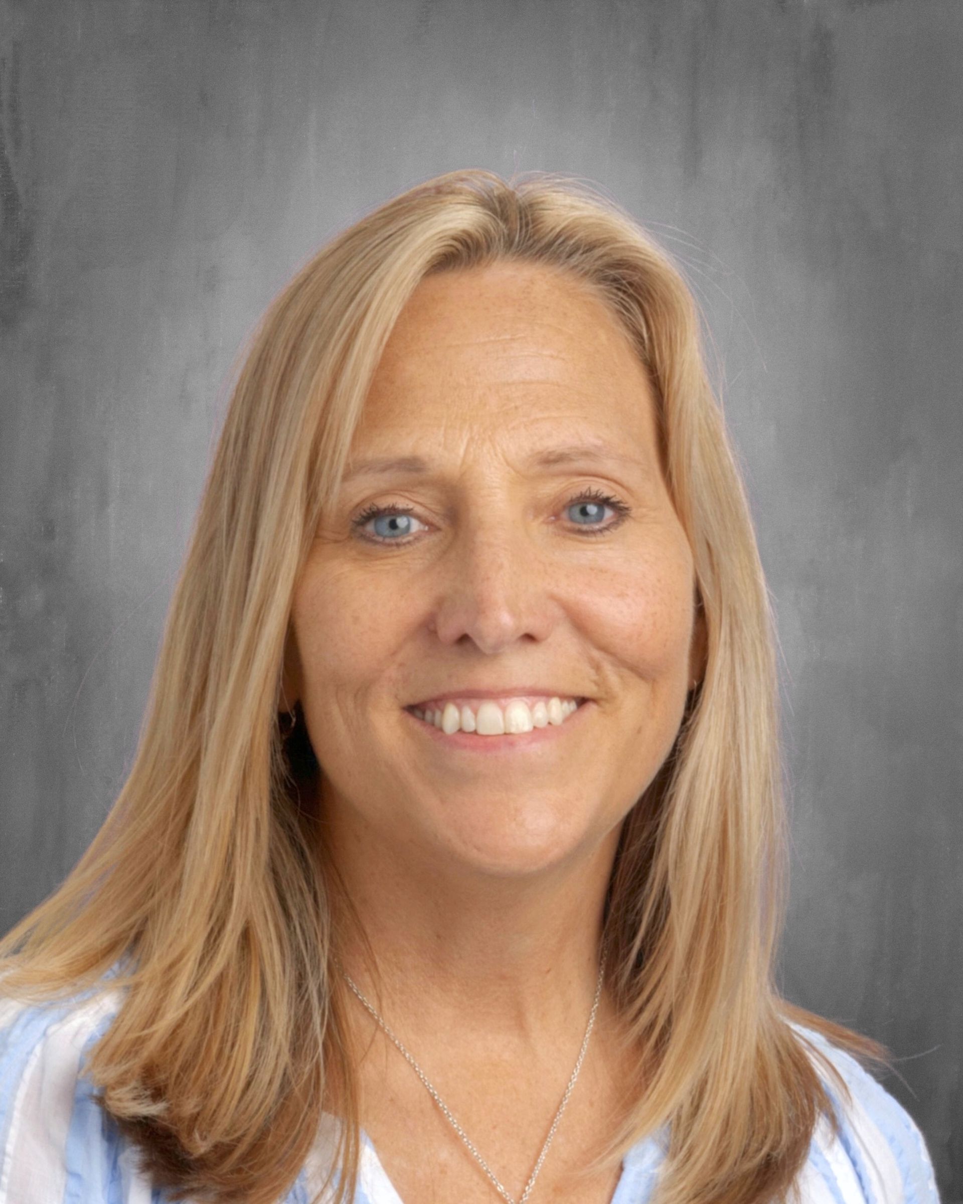 Blonde woman smiling at camera; light blue striped shirt, gray background.