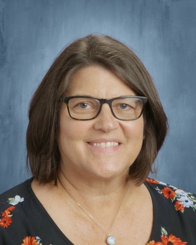 Woman with glasses smiles, wearing a dark shirt with orange floral pattern. Blue background.