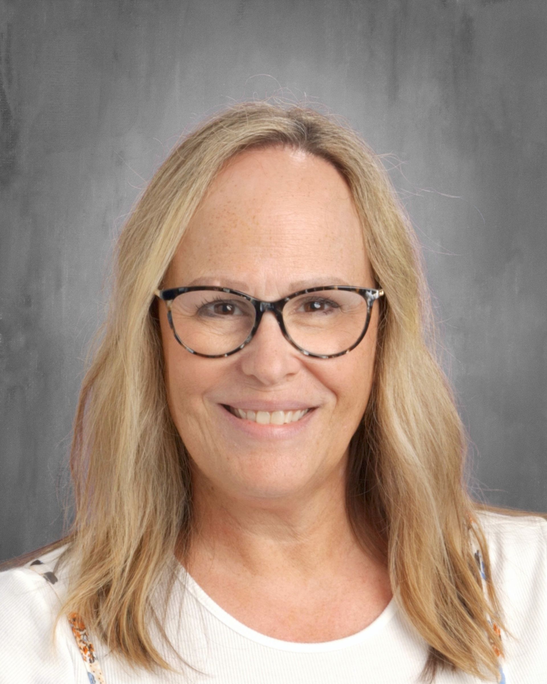 Woman with blonde hair and glasses smiles at the camera, against a gray backdrop.