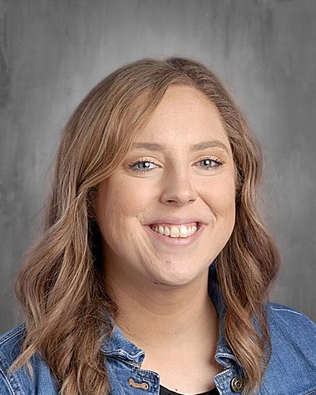 Woman with graying curly hair smiles; neutral background.