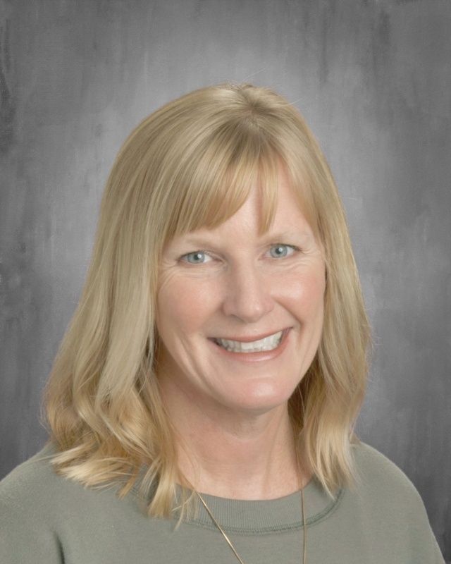 Blonde woman with a warm smile; wearing a green shirt against a gray background.