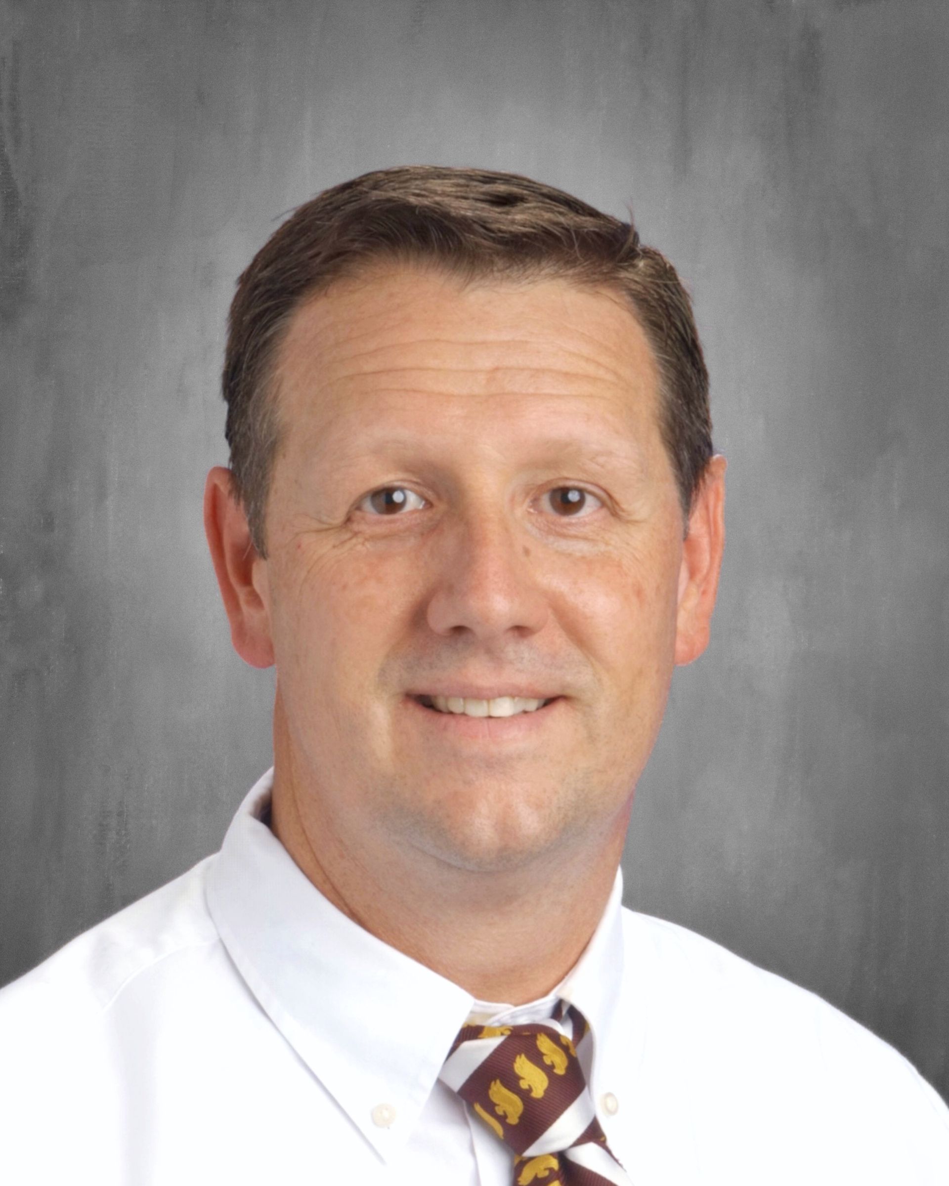 Man in white shirt and tie smiles at the camera, against a gray background.