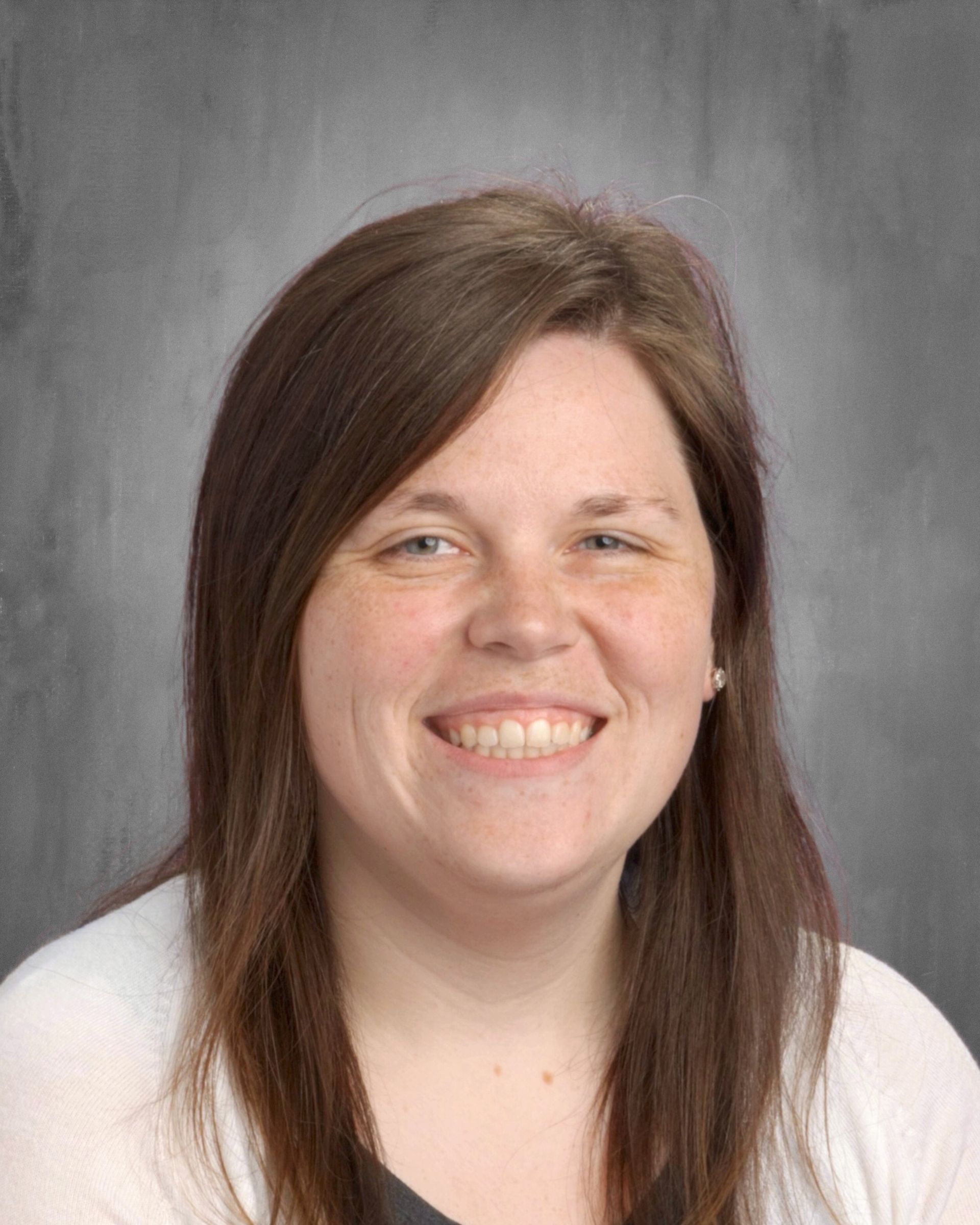 Woman with brown hair smiles, wearing a white sweater, against a gray backdrop.