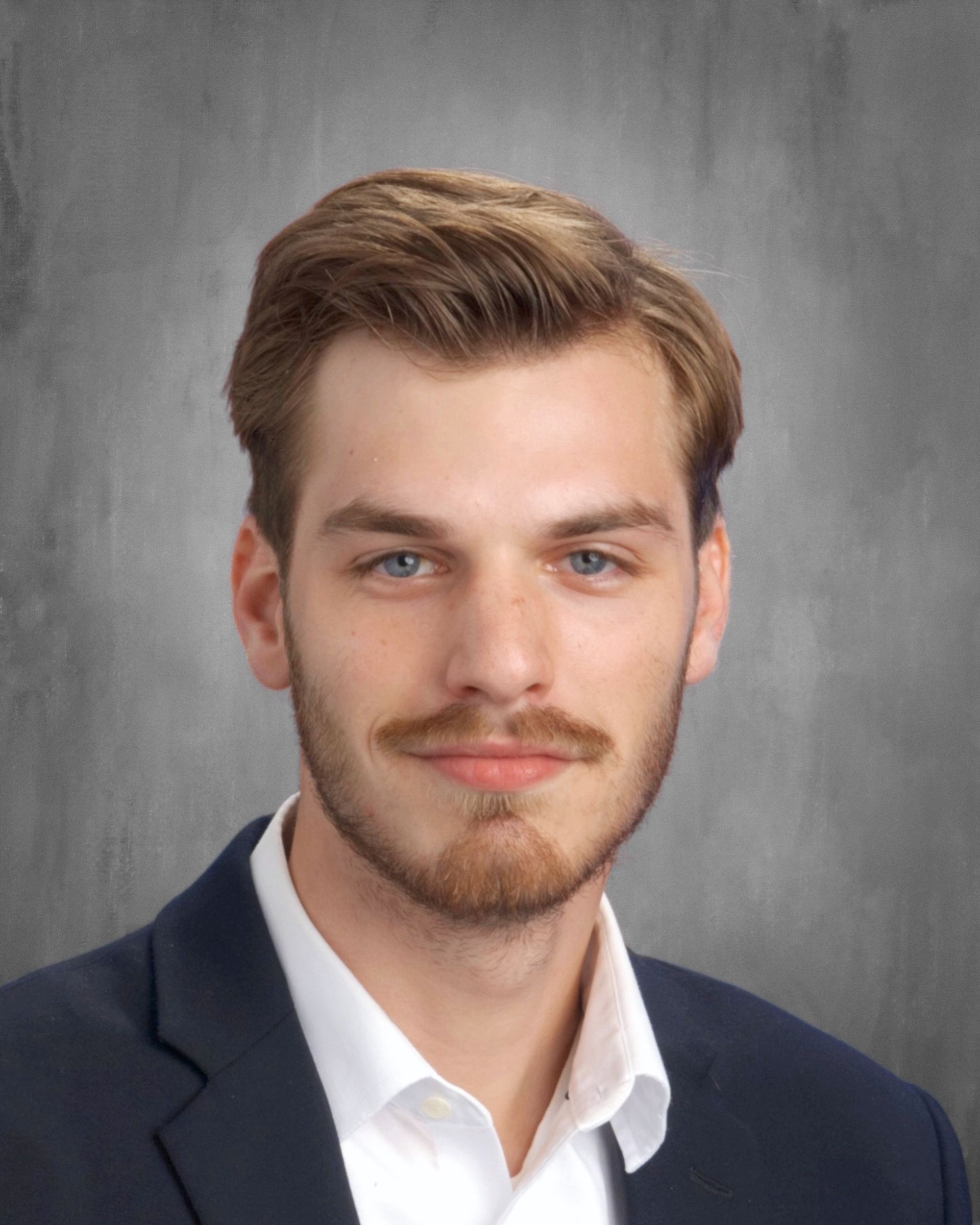Young man with light brown hair and stubble wearing a blazer and white shirt; looking at the camera.