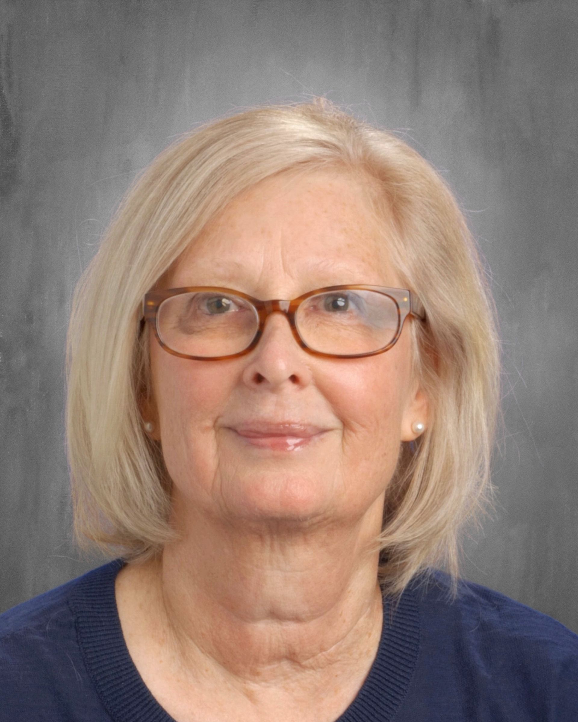 Woman with blonde hair and glasses, smiling at the camera. Grey background.