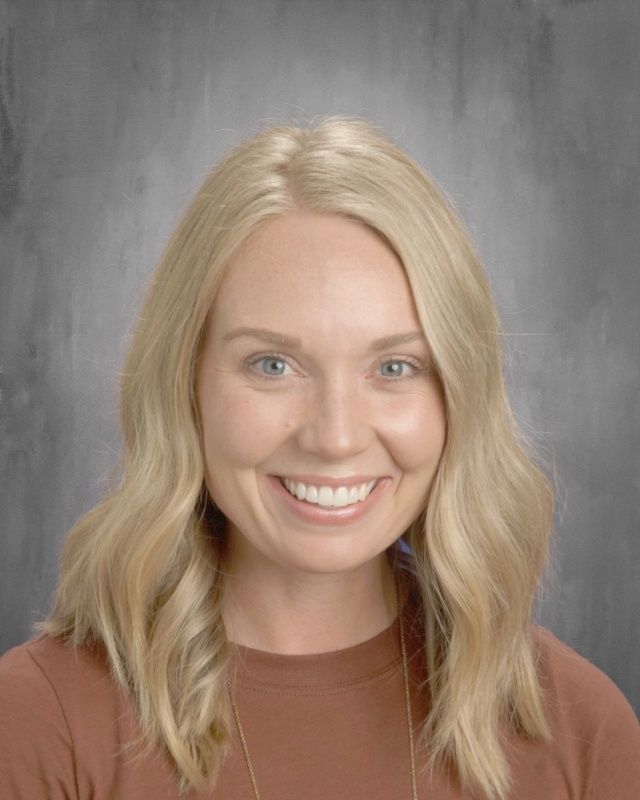 Blonde woman smiling, brown shirt, neutral gray background.