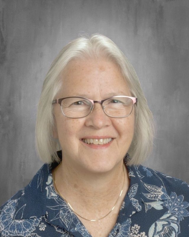Woman with glasses, smiling, wearing a blue floral shirt, against a gray background.