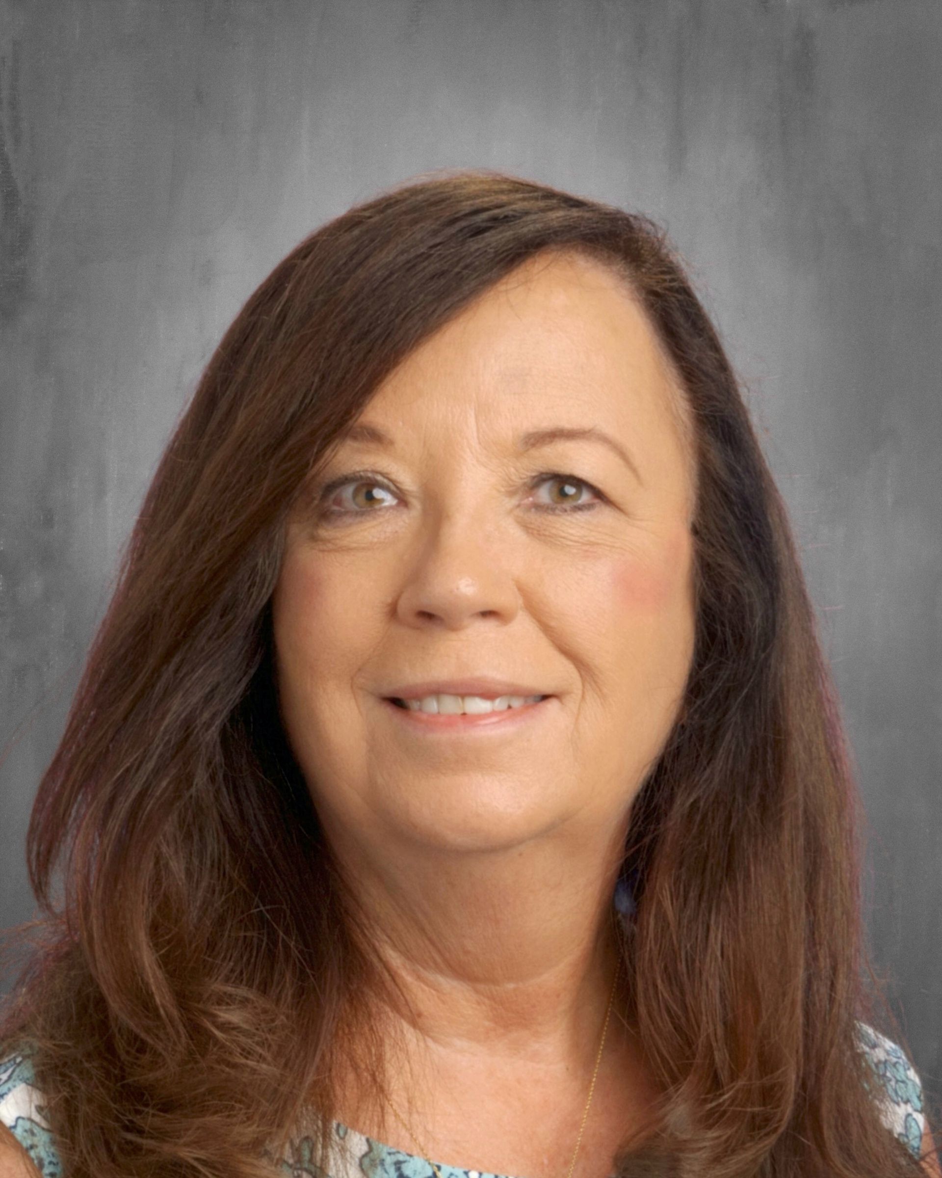 Woman with brown hair smiles at the camera in front of a gray backdrop.