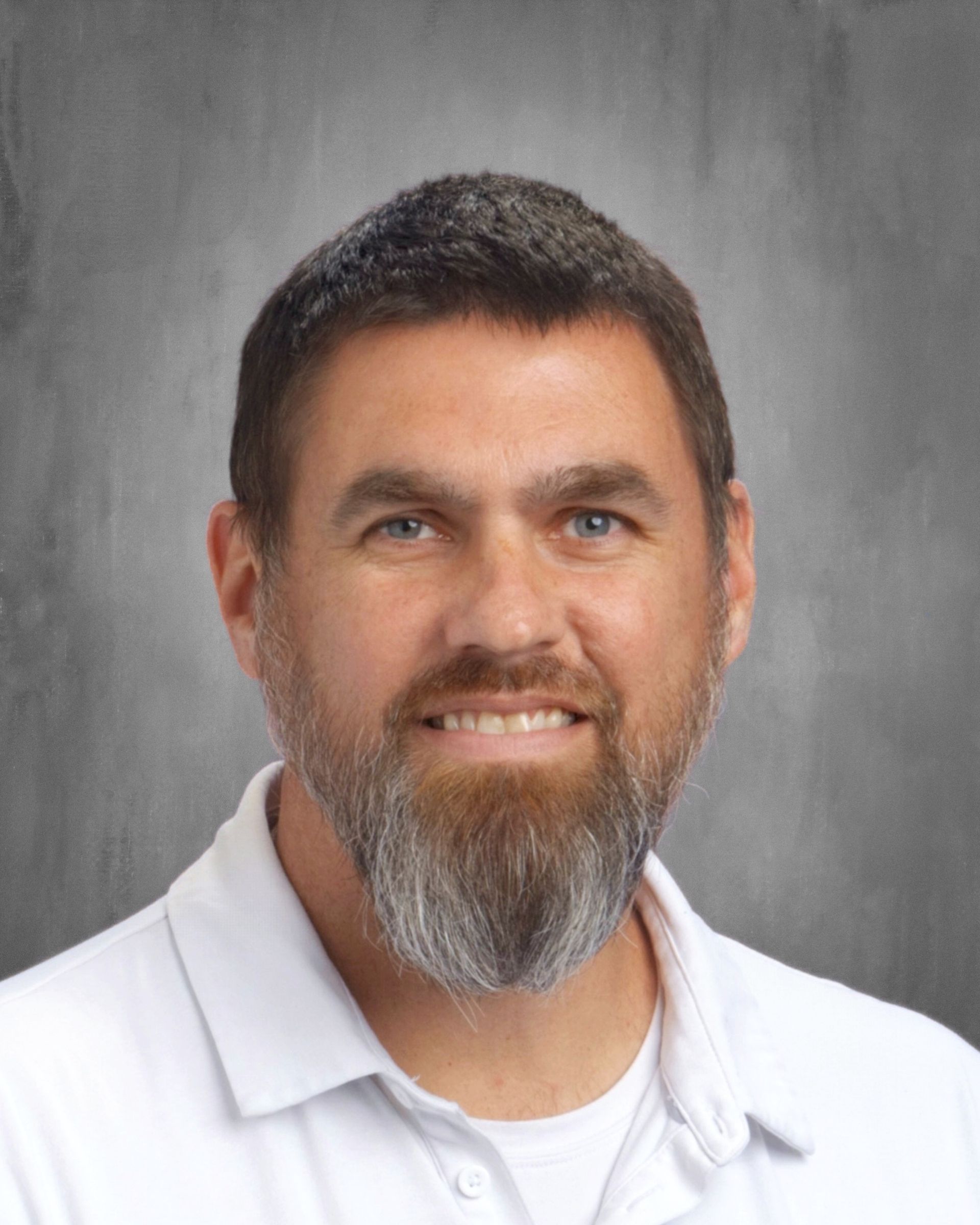 Man with beard, smiling, wearing white polo shirt, against a gray background.