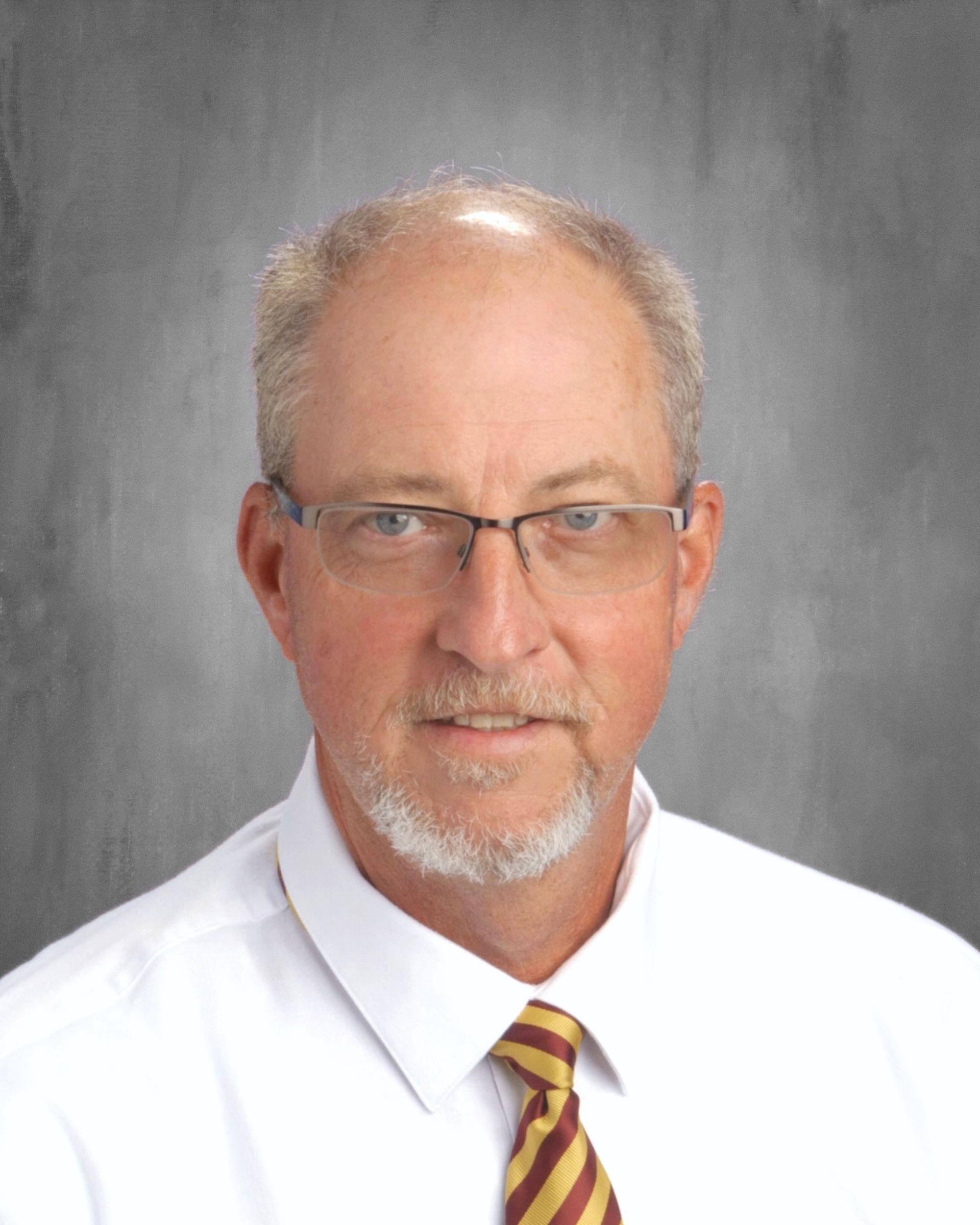 Man with glasses, white shirt, and gold tie, looking at the viewer with a neutral expression.
