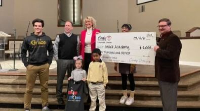 People holding a large check at a church, likely a donation to an academy.