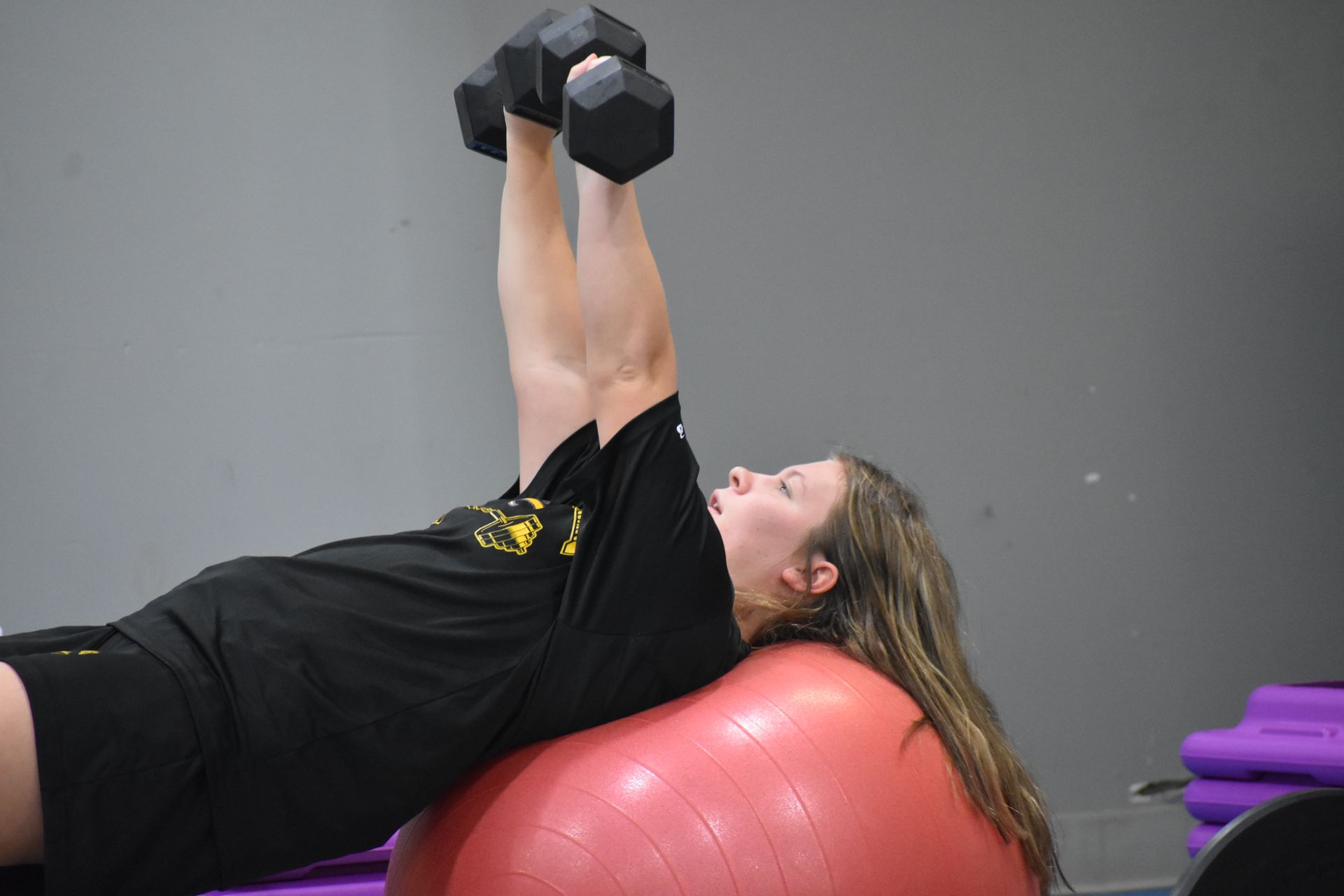 Woman on a fitness ball doing dumbbell chest presses in a gym.