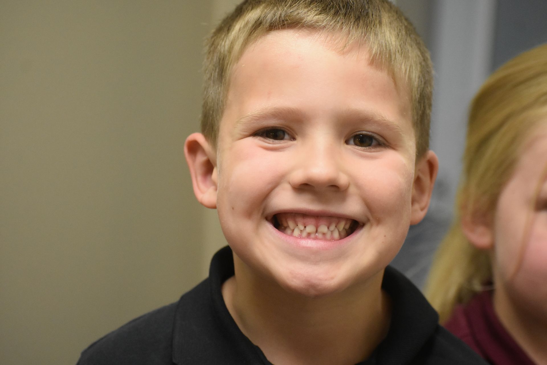 Smiling young boy with blonde hair, dark shirt.