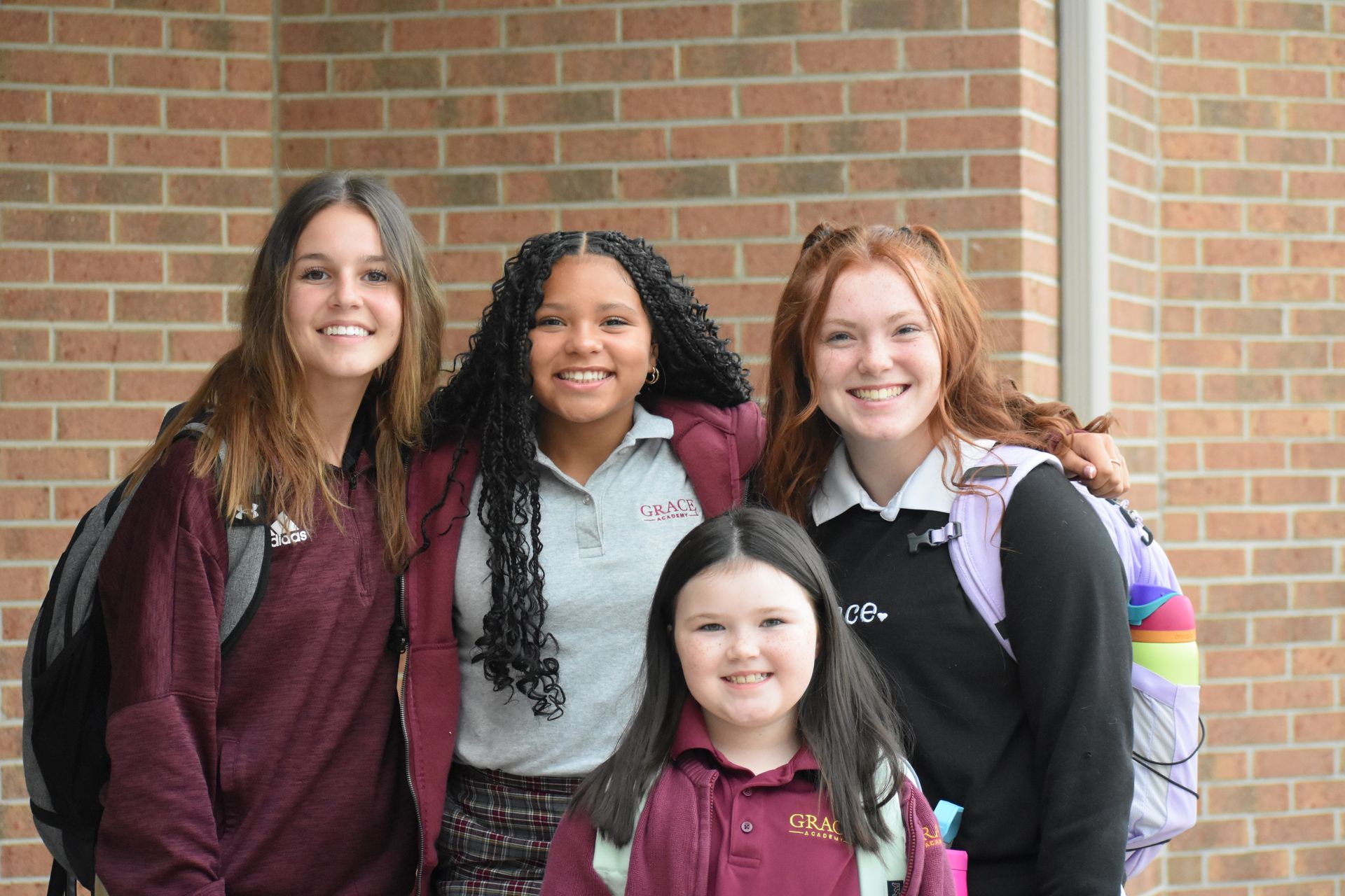 Four smiling students, standing outside a brick building.