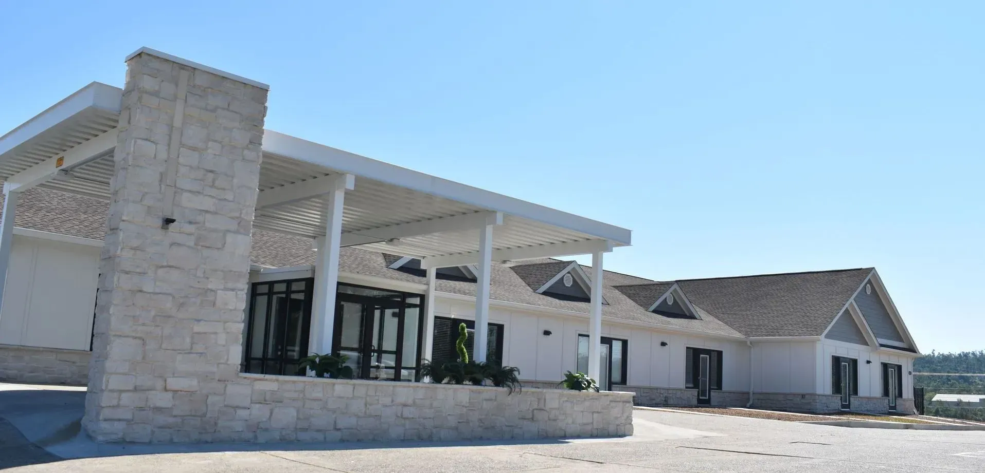 Modern white building with stone accents and a covered entrance under a blue sky.
