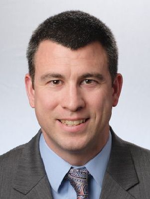 Man in a suit smiling at the camera, medium close-up, studio setting.