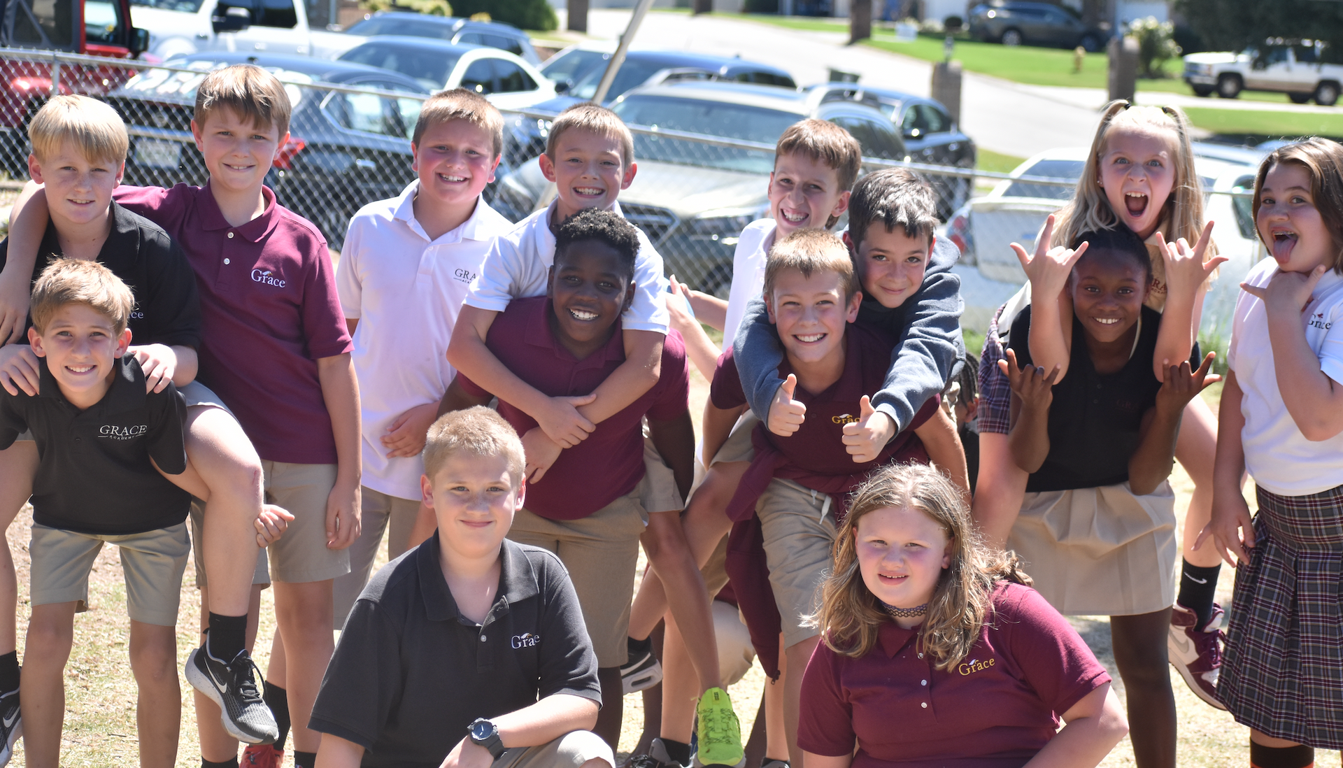 Children in school uniforms smile and pose outdoors, some on others' shoulders.