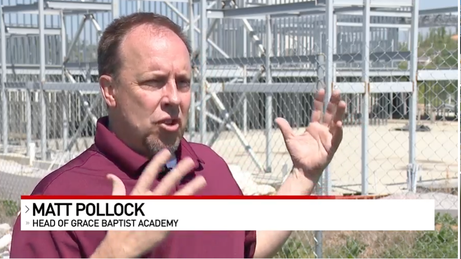 Matt Pollock, Head of Grace Baptist Academy, speaks with hands raised, outdoors near construction.