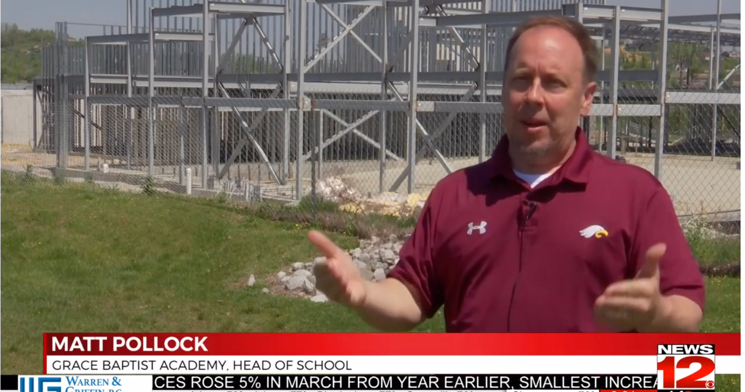 Matt Pollock, Head of School at Grace Baptist Academy, speaks outdoors. Metal bleachers are behind him.