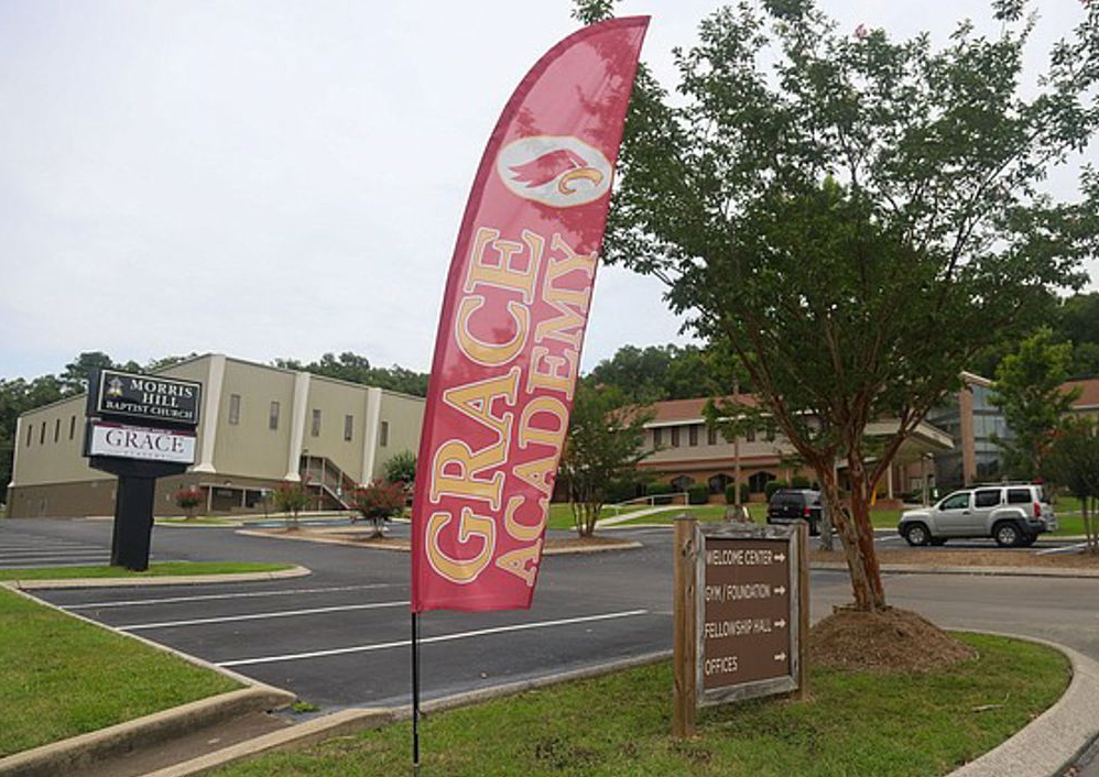 Grace Academy flag in front of a school building on a cloudy day.