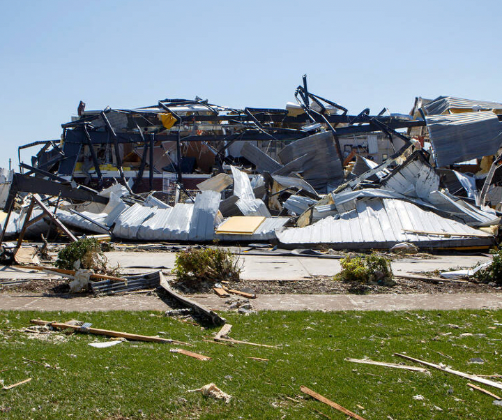 Debris of a building destroyed by a storm, metal and wood scattered on grass and pavement.