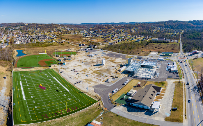 Aerial view: football and baseball fields, construction site, power station, road, houses in the distance, sunny day.