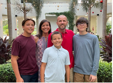 Family of five posing outdoors: mother, father, and three sons smiling at the camera.