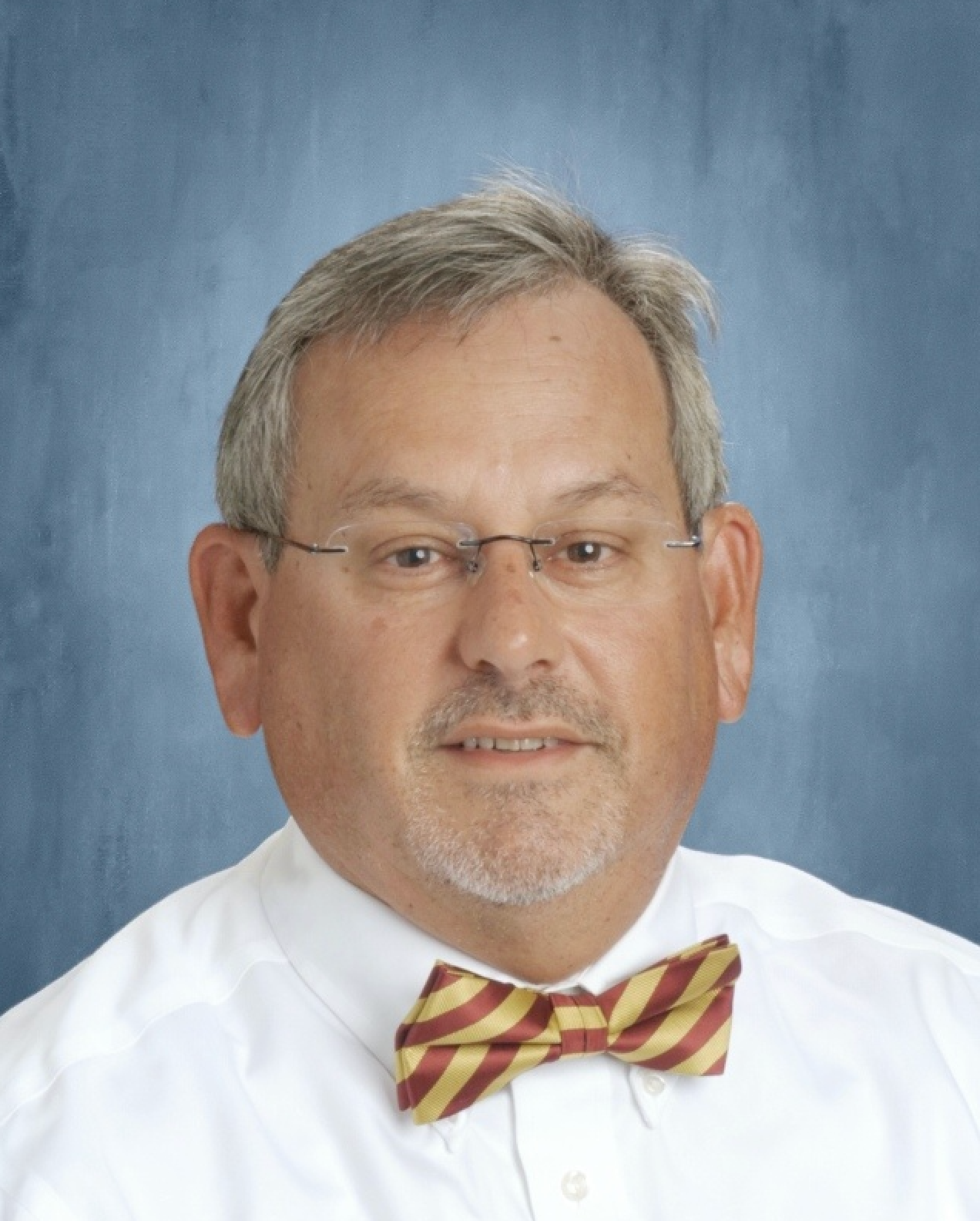 Man with glasses and bow tie, smiling against a blue background.