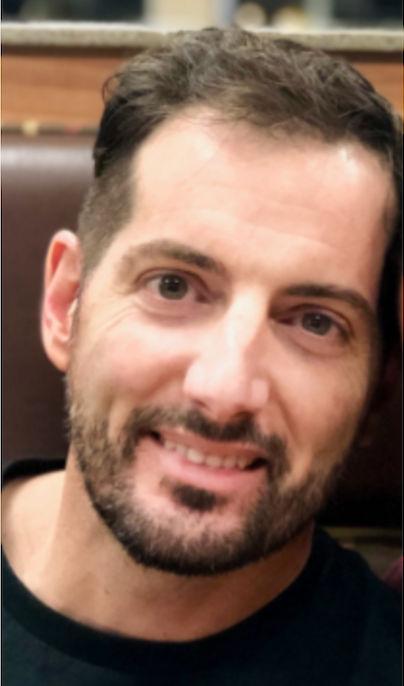 Man with dark hair and stubble smiles at the camera.