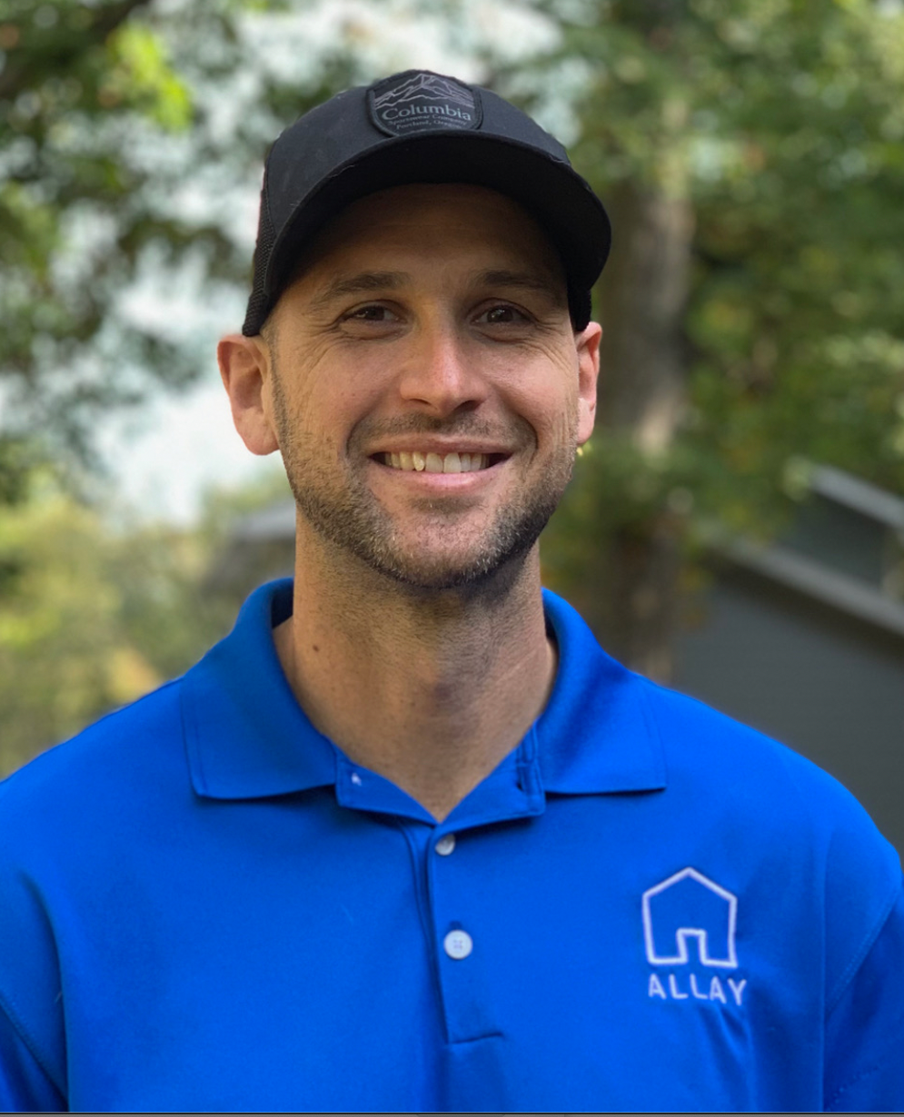 Man wearing a black cap and blue shirt with a logo, smiling outdoors.