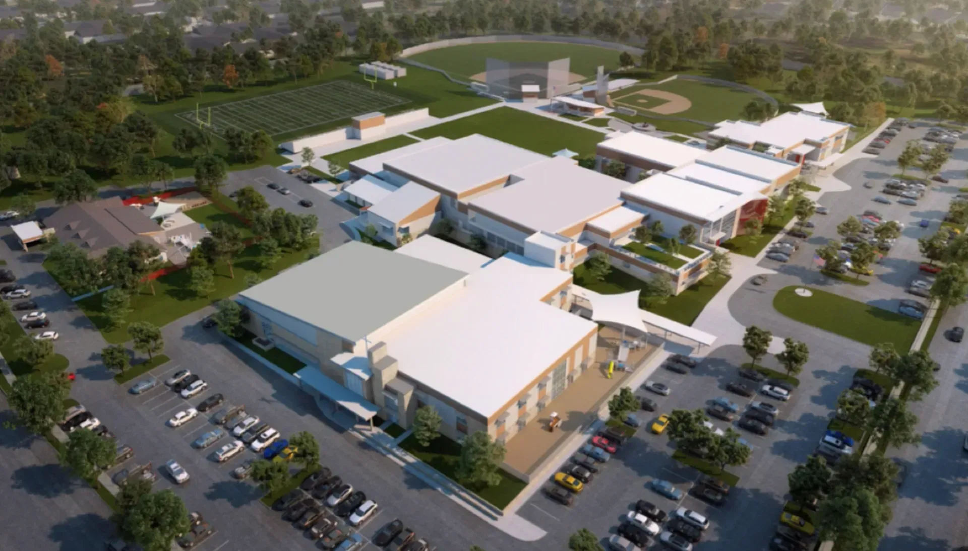 Aerial view of a large school complex with parking, sports fields, and multiple buildings, set in a green, suburban area.