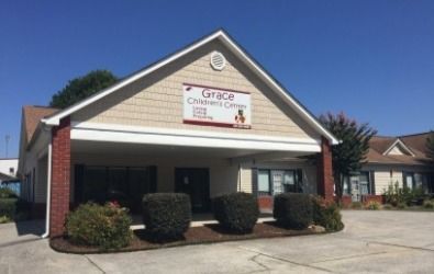 Grace Children's Center building with tan siding, red brick accents, and a small sign on a sunny day.