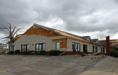 Damaged building with missing roof and siding, cloudy sky.