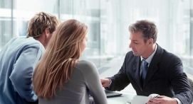 A financial advisor in a suit consults with a couple at a desk in an office.