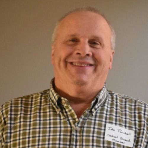 Smiling older man with thinning hair, wearing a plaid shirt. He is identified as John Parshall, School Branch Member.
