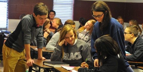 Students collaborate in a classroom setting, looking at papers on a desk.