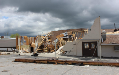 Building severely damaged, partially collapsed, after a storm. Dark gray clouds in the background.
