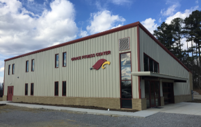 Grace Fitness Center, a tan and red metal building with large windows and a logo of a red bird, against a blue sky.