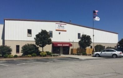 A dance academy in a white building with a red awning, parking lot, and a car.