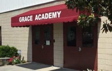 Red awning over Grace Academy entrance, featuring two brown doors and a tan brick wall.