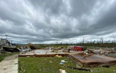 Tornado damage: Foundation of destroyed home on grass, debris scattered, dark sky overhead.