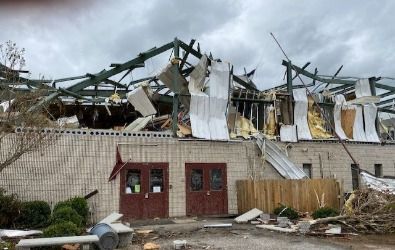 Building with roof and walls torn apart, debris scattered outside. Gray sky, brown doors.