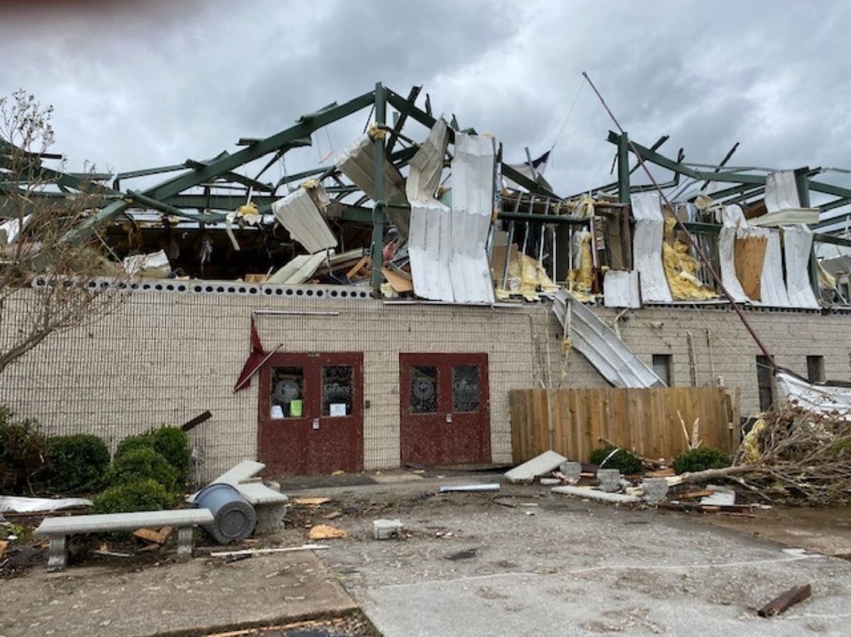 Building with severe roof damage after a storm, debris scattered around the entrance.
