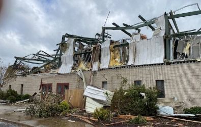 Building with severe roof damage after a storm; torn metal and debris visible.