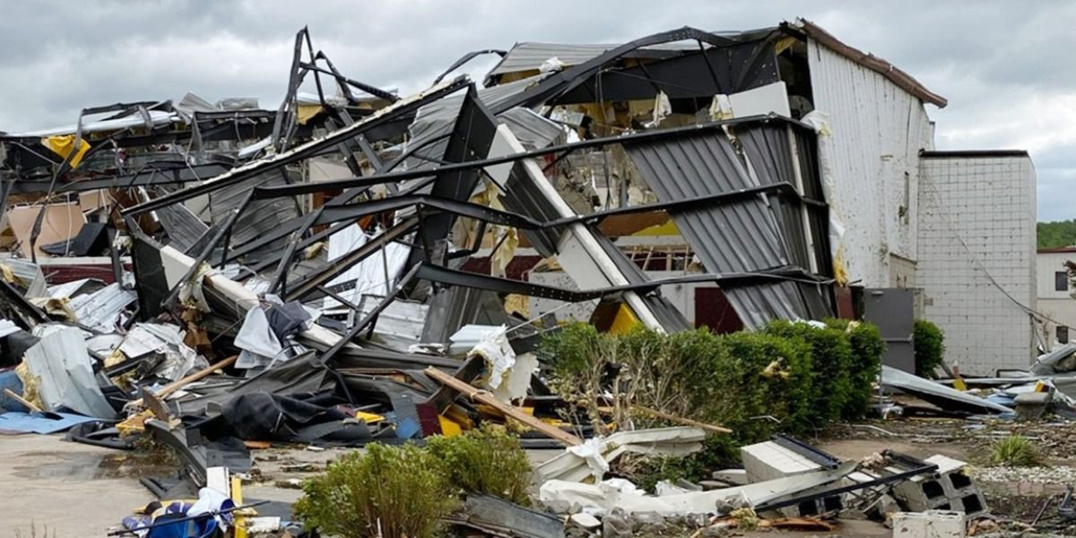 Building severely damaged; collapsed roof and walls. Debris covers the ground. Overcast sky.
