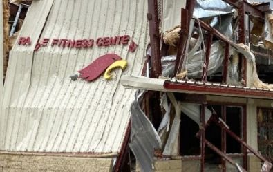 Rage Fitness Centre sign on a severely damaged building after a disaster; red and yellow logo.